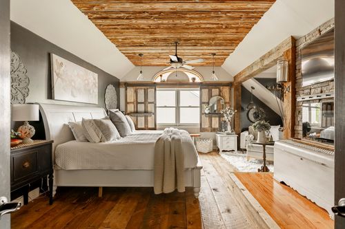 Primary bedroom with a white sleigh bed beneath a wood beam vaulted ceiling and reclaimed wood shutters