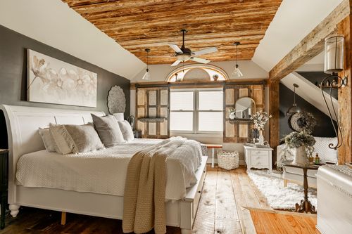 Primary bedroom with a white sleigh bed, wood beam ceiling, and an arched window with wood shutters