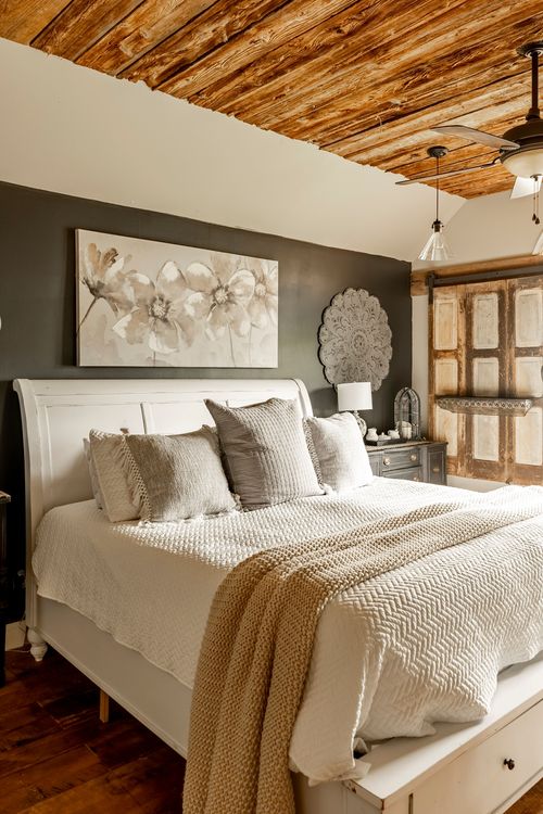Primary bedroom with a dark accent wall, floral art, white bed, and reclaimed wood door accent