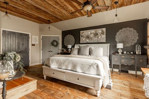 Primary bedroom with a wood beam ceiling, dark accent wall, medallion art, and white storage bed