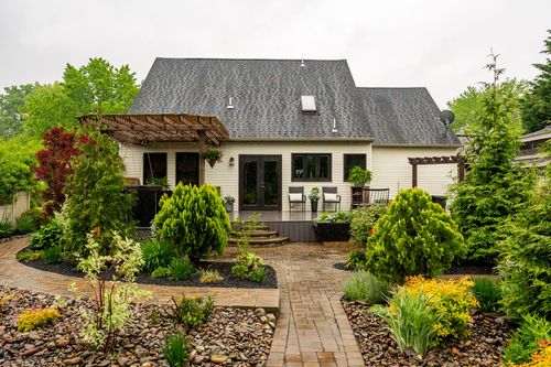Backyard patio with a wood pergola, paver walkway, and curved landscaped garden beds