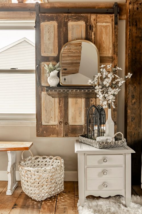 Reclaimed wood barn door vignette with a mirror, floral arrangement, and white nightstand