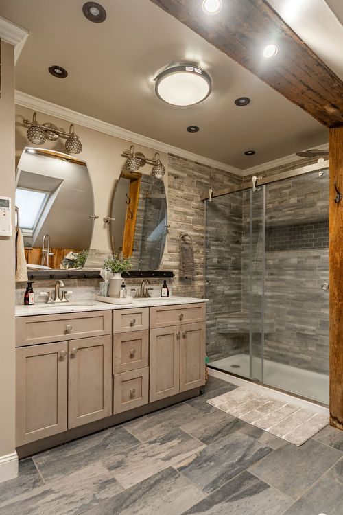 Primary bathroom with a double vanity, oval mirrors, tile walk-in shower, and a skylight