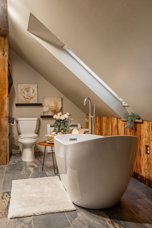 Primary bathroom with a freestanding soaking tub beneath a sloped skylight and wood plank accent wall