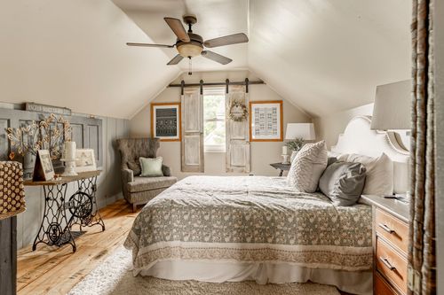 Bedroom under a sloped ceiling with reclaimed wood shutters, a wingback chair, and patterned bedding