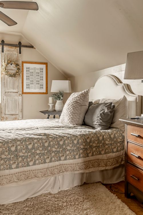 Bedroom with an upholstered headboard, sloped ceiling, reclaimed barn door, and patterned quilt