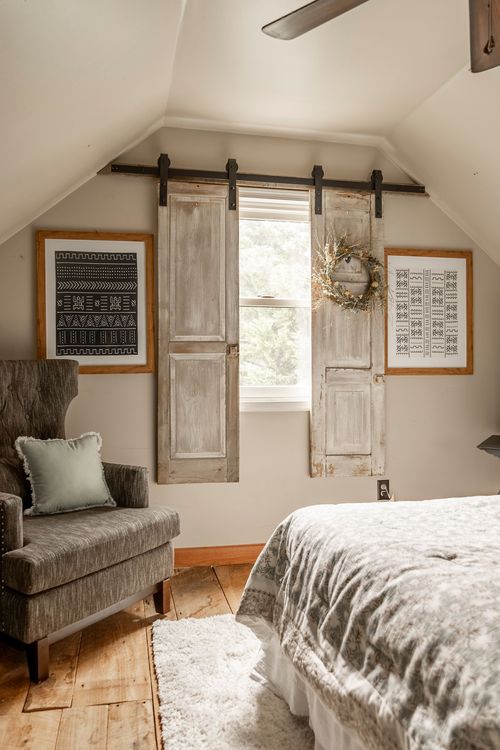 Bedroom corner with reclaimed wood shutters flanking a window and a tufted gray armchair