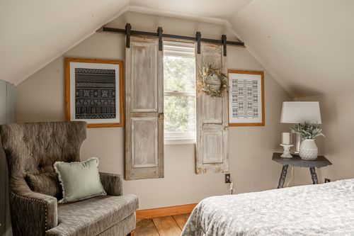 Cozy attic bedroom with vintage barn-door shutters over the window and a tufted armchair