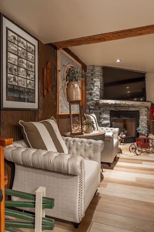 Cozy den with tufted linen sofas, striped pillow, stone fireplace and a reclaimed wood beam