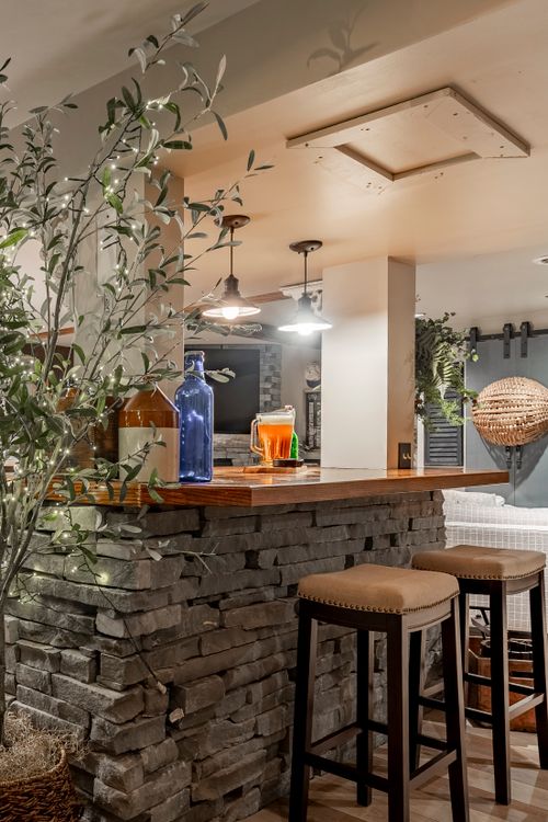 Stone-front bar with pendant lighting, potted olive tree, blue bottles and leather barstools