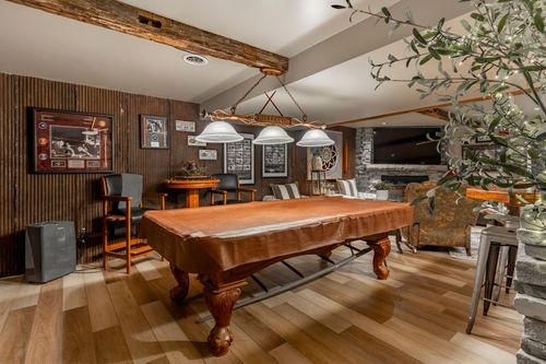 Basement game room with a pool table, drum pendant lights, wood beam ceiling and stone fireplace