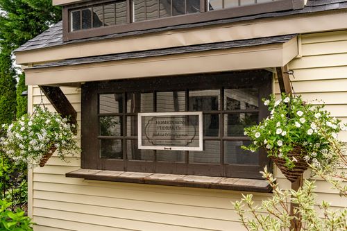 Bay window sign reading Hometown Floral Co. flanked by hanging flower baskets on a cream house exterior