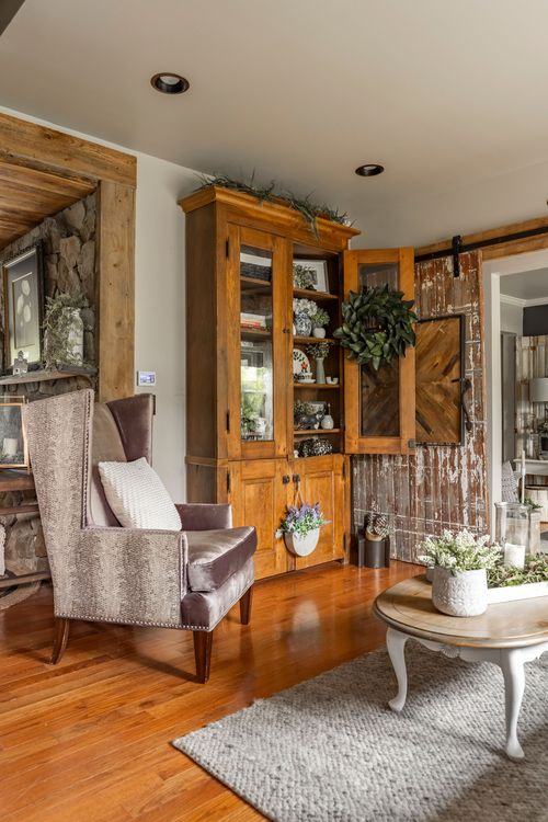 Living room corner with a wingback chair, wood hutch styled with a wreath, and sliding barn doors