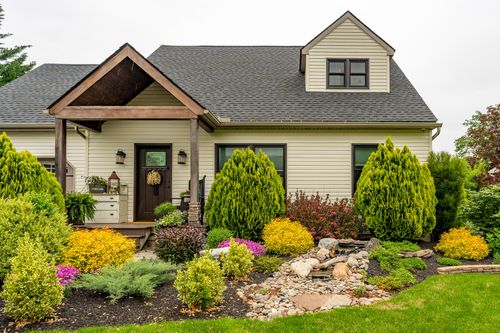 Close-up of a home's wood gable entry porch with dark front door, wreath, and layered plantings