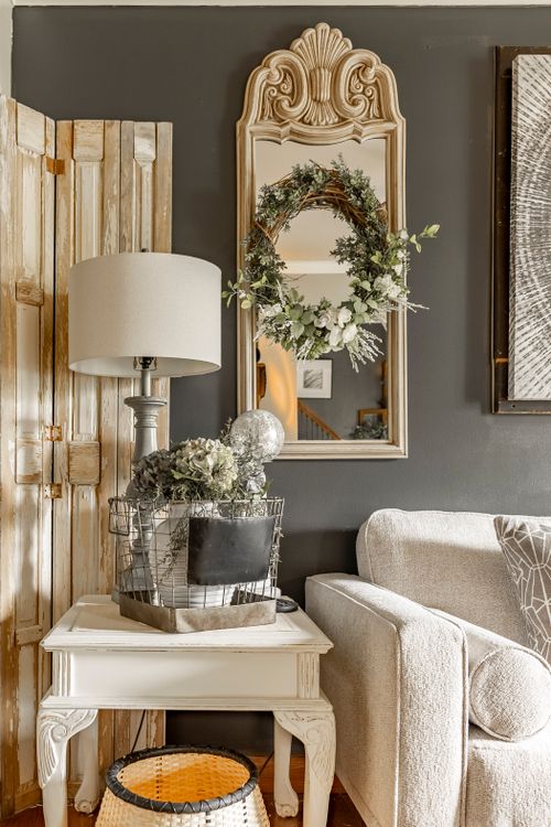 Corner vignette with a wood folding screen, ornate wreathed mirror, and a cream armchair