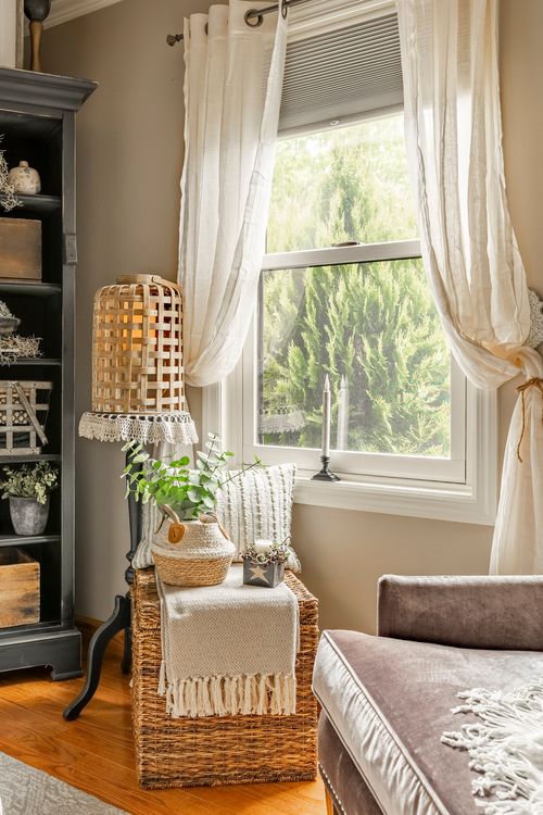 Reading nook with a woven basket ottoman, textured pendant lamp, and a window framed in sheer curtains