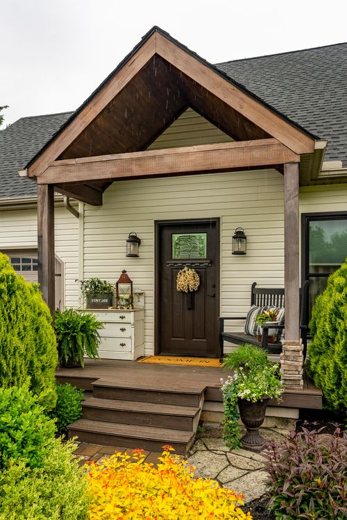 Covered front porch with a dark door, wreath, lanterns, and a decorative dresser accent piece