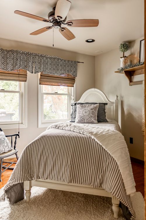 Bedroom with a white bed dressed in striped ticking bedding beneath a ceiling fan