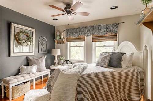 Bedroom with a dark accent wall, wreathed mirror, bench, and white bed with striped bedding