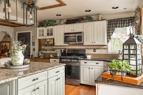Sage green kitchen island with granite counters and a stainless range in a farmhouse kitchen