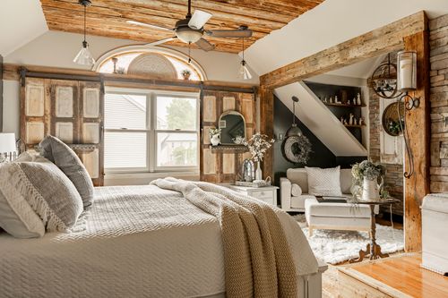Primary bedroom with wood plank ceiling, reclaimed shutters, and a sitting area near open stairs