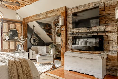 Bedroom with a stacked stone fireplace wall, mounted TV, and a white blanket chest