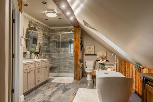 Primary bathroom with a glass walk-in shower, wood vanity, and freestanding soaking tub under sloped ceilings