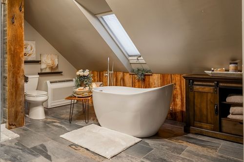 Primary bathroom with a freestanding tub, wood plank wall, sloped skylight, and dark wood cabinet