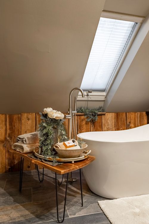 Bathroom vignette with a freestanding tub, floor-mount faucet, and a wood side table styled with towels