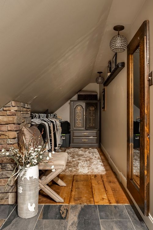 Attic closet with a stacked stone accent, open clothing rack, dark armoire, and tall mirror