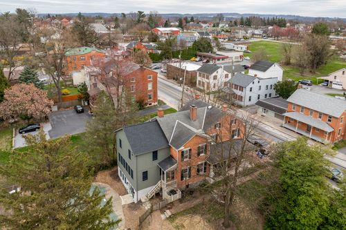 Aerial view of a small-town block with a red-brick home and gray addition among tree-lined streets