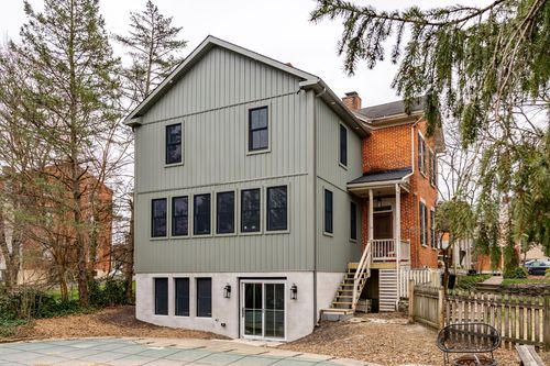 Gray addition exterior with wood deck stairs, black windows and a red-brick historic house attached