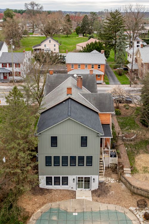 Aerial view of a gable-roofed brick-and-gray home addition among tree-lined village rooftops