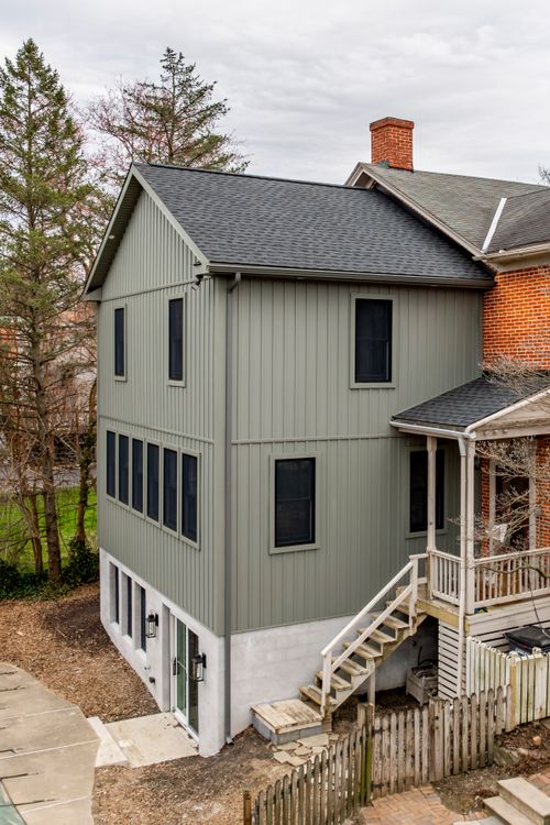 Gray gabled addition beside a brick house with a screened porch and wood staircase to the yard