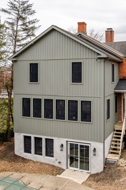 Symmetrical rear elevation of a gray board-and-batten addition with a brick chimney behind it