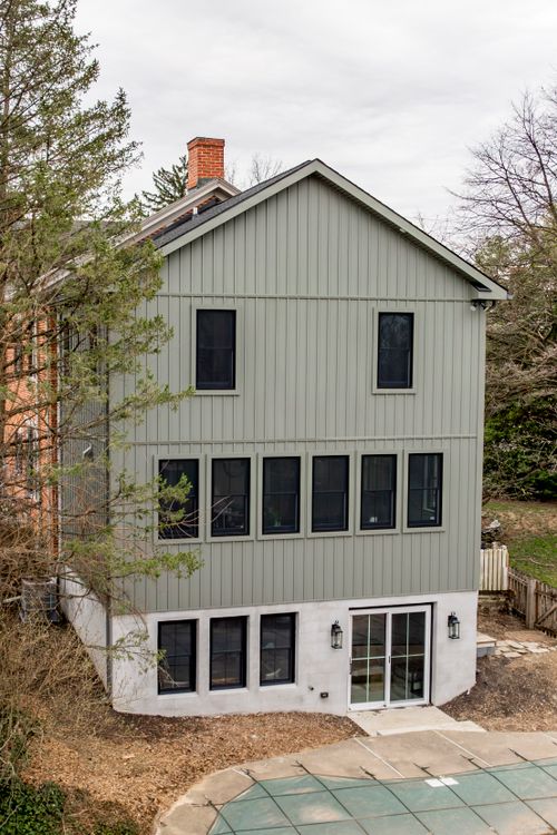 Gray addition exterior framed by evergreen trees with a wood privacy fence along the yard