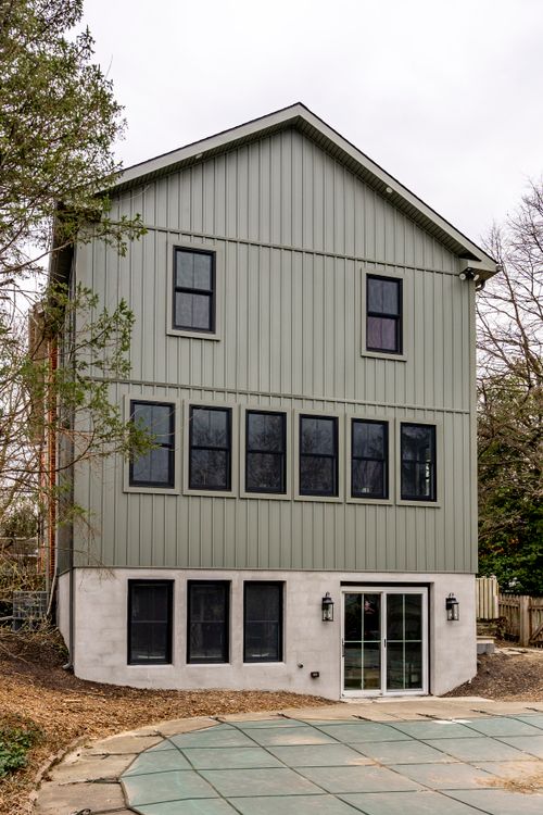 Gray board-and-batten addition with grid windows and a brick chimney over the roofline