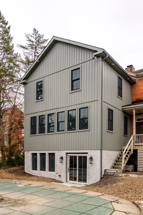 Gray home addition with wood deck stairs, a covered brick porch and a covered pool below