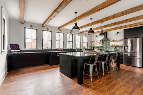 Long black kitchen with exposed wood beams, gray quartz island and a wall of multi-pane windows