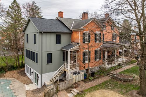 Aerial view of a gray-and-brick village home with a covered side porch and in-ground pool