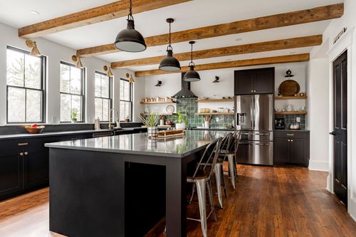 Black kitchen with green tile backsplash, wood ceiling beams and a long gray quartz island