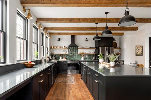 Kitchen with green tile backsplash, black vent hood and open wood shelving under beamed ceiling