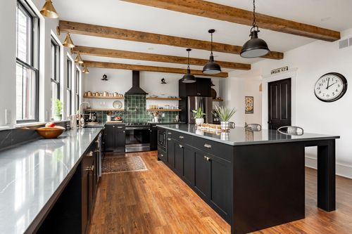 Kitchen with black cabinetry, gray quartz counters, a wall clock and paneled black door