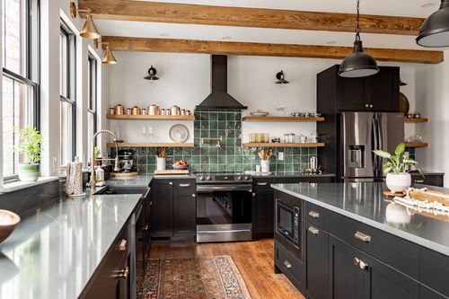 Kitchen with black range, copper cookware and open wood shelving against green tile