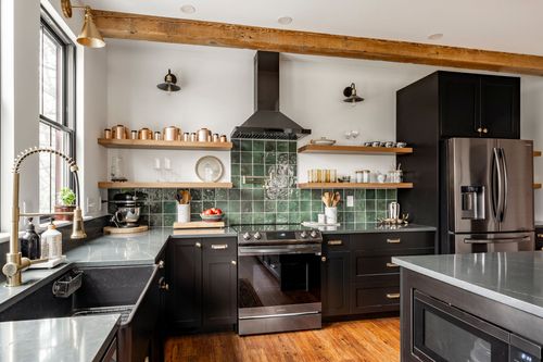 Close view of a black kitchen range with copper pots, gooseneck faucet and green tile backsplash