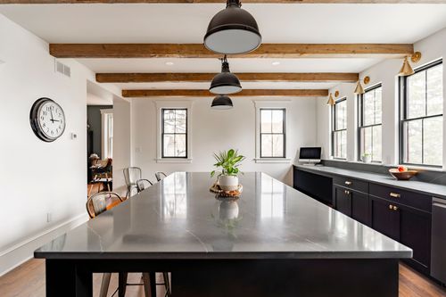 Kitchen island with a gray soapstone counter, wood beam ceiling and dining nook beyond