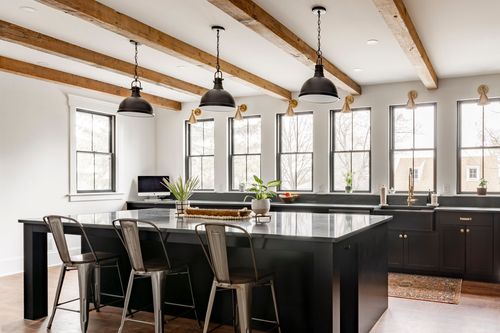 Kitchen island with metal barstools, black pendant lighting and a row of windows under wood beams