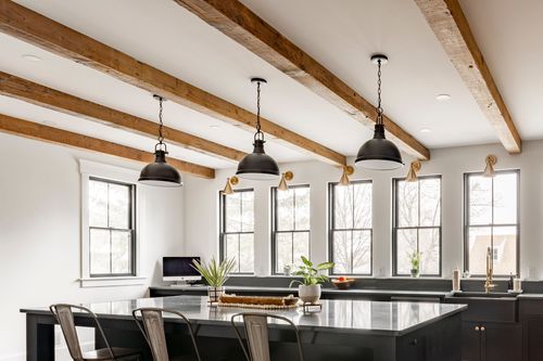 Kitchen island area with black pendant lights, exposed wood beams and a wall of windows