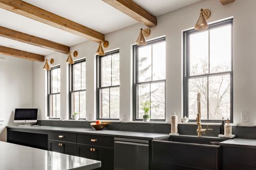 Kitchen counter with a black farmhouse sink, brass gooseneck faucet and brass wall sconces