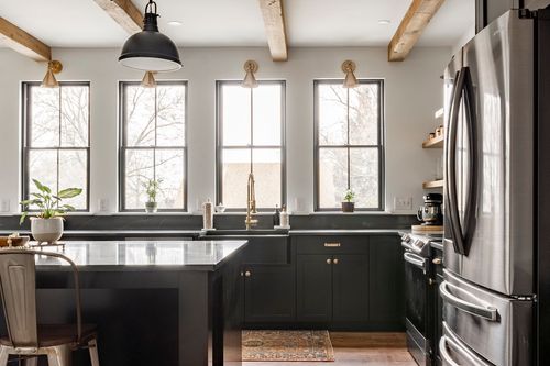 Kitchen with black cabinetry, farmhouse sink, brass fixtures and wood beam ceiling